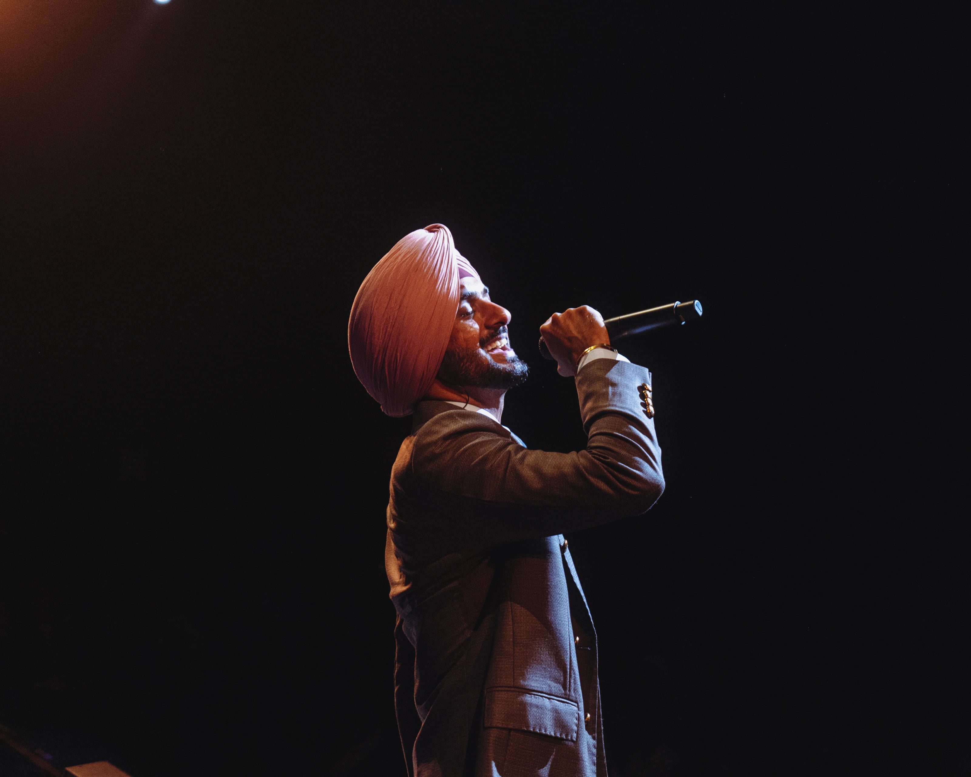 A singer in a turban holds a microphone against a dark stage.