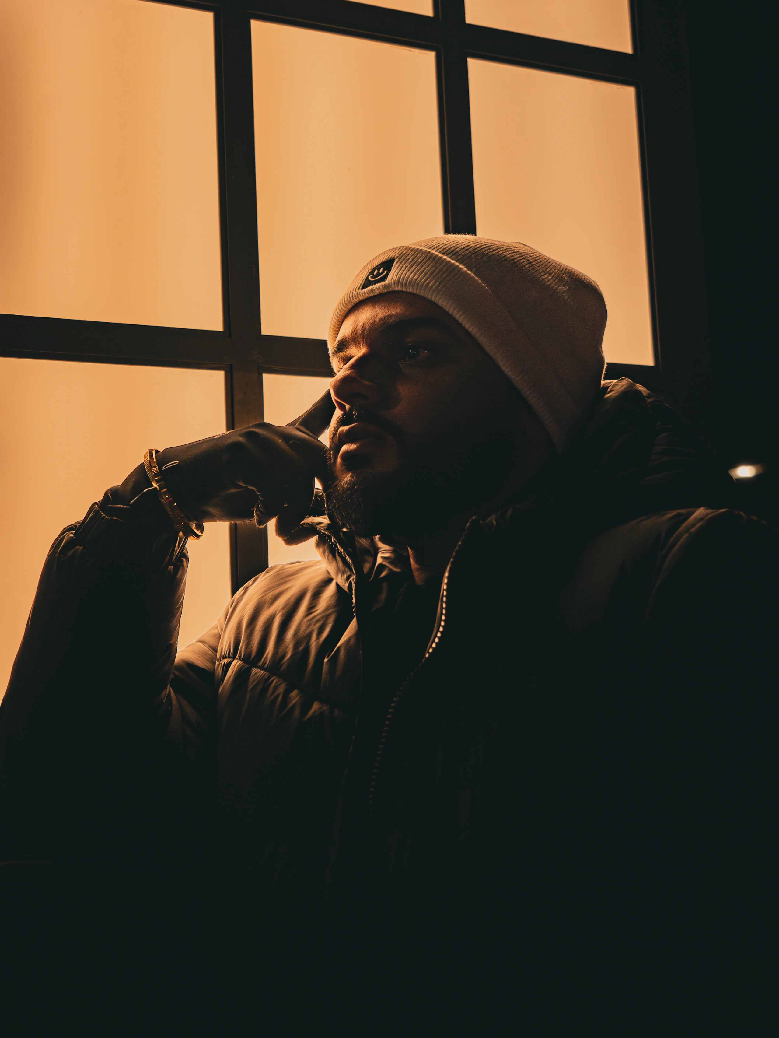 A person in a knit hat and jacket sits beside a glowing window.
