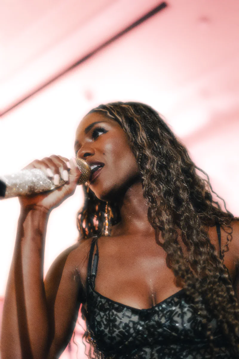 A singer performs into a sparkling microphone under pink light.