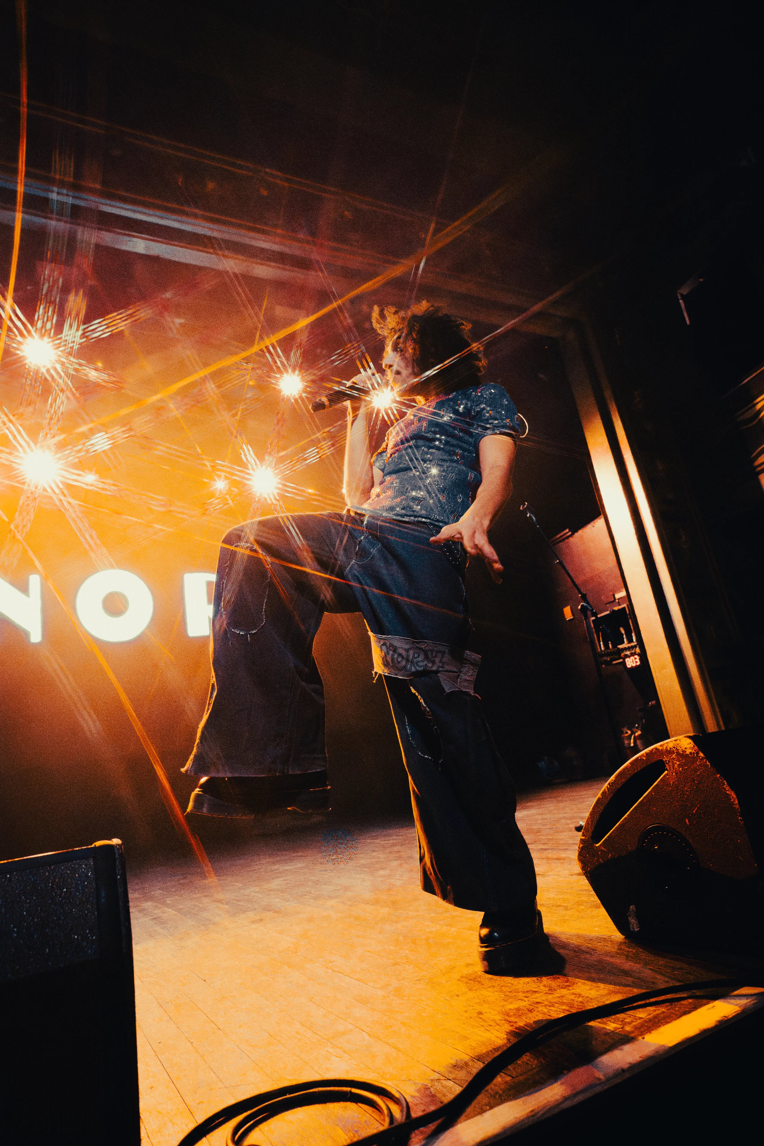 A performer sings into a microphone onstage beneath bright orange lights.