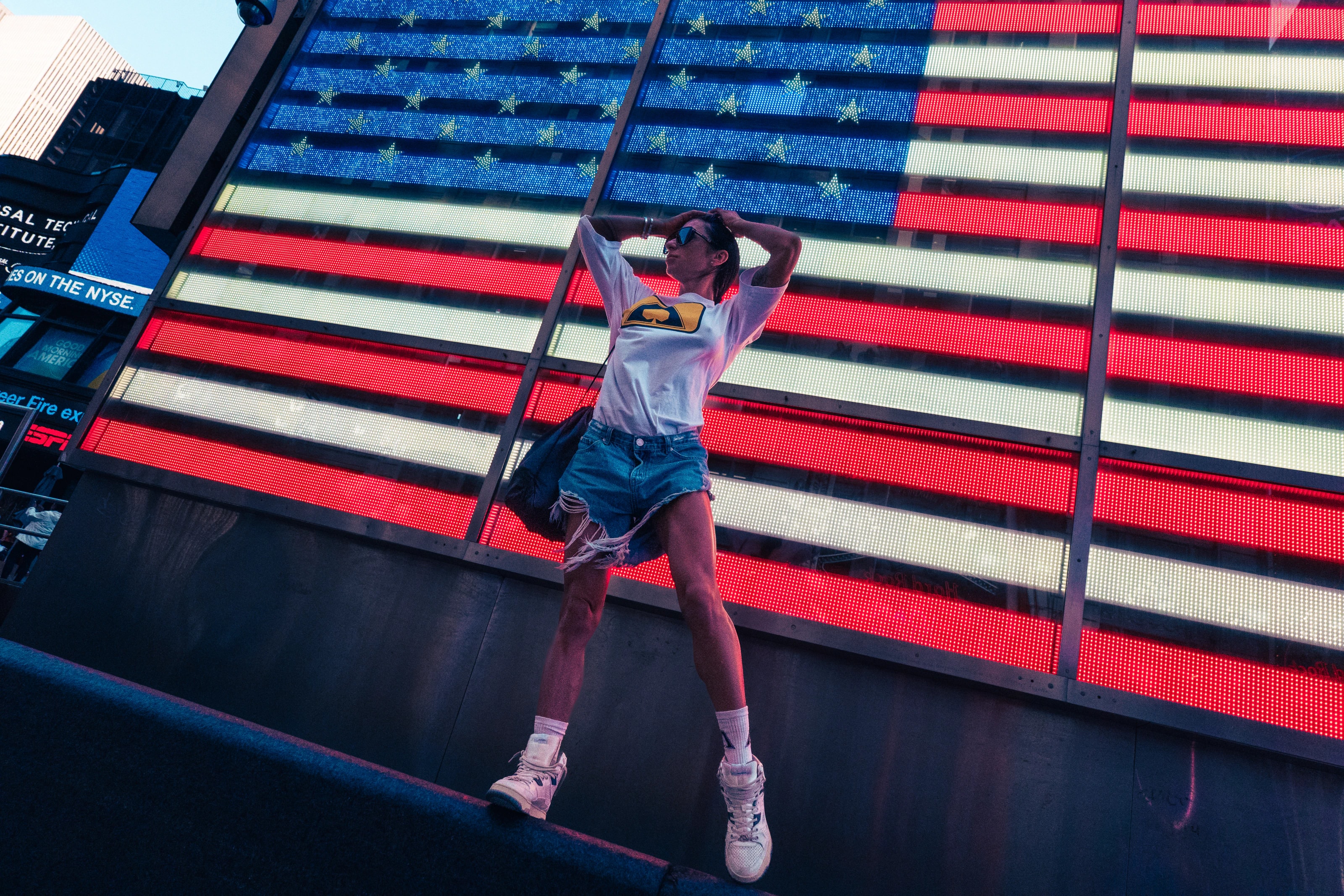 A person poses in front of a large American flag LED display.