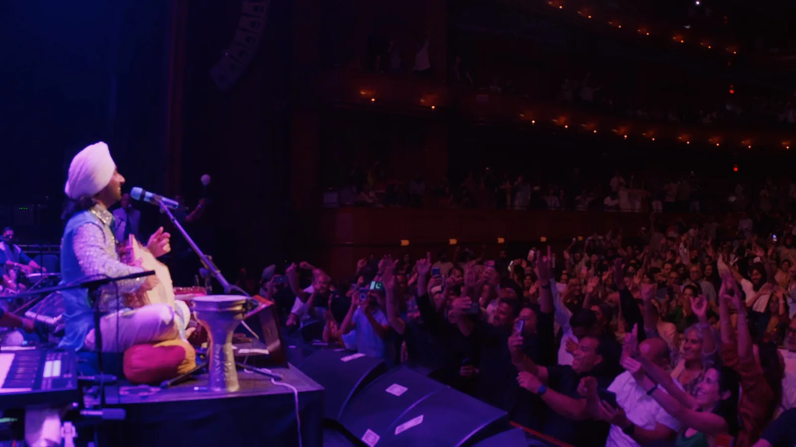Satinder Sartaaj performs onstage for an audience in a theater.